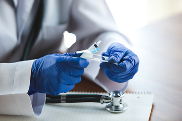 Image showing Close up of doctors hands wearing blue protective gloves with stethoscope and syringe on wooden table background