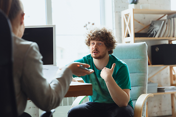 Image showing Young man sitting in office during the job interview with female employee, boss or HR-manager, talking, thinking, looks confident