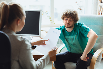 Image showing Young man sitting in office during the job interview with female employee, boss or HR-manager, talking, thinking, looks confident