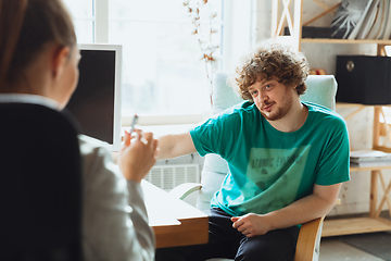 Image showing Young man sitting in office during the job interview with female employee, boss or HR-manager, talking, thinking, looks confident