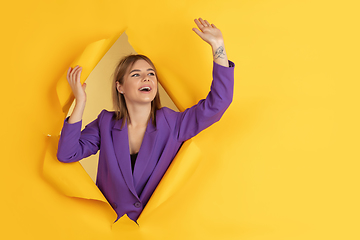 Image showing Cheerful young woman poses in torn yellow paper hole background, emotional and expressive