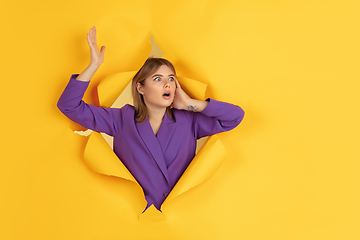 Image showing Cheerful young woman poses in torn yellow paper hole background, emotional and expressive