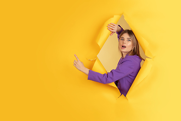 Image showing Cheerful young woman poses in torn yellow paper hole background, emotional and expressive