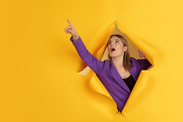 Image showing Cheerful young woman poses in torn yellow paper hole background, emotional and expressive