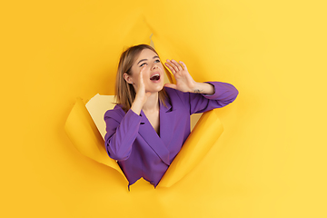 Image showing Cheerful young woman poses in torn yellow paper hole background, emotional and expressive