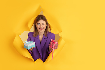 Image showing Cheerful young woman poses in torn yellow paper hole background, emotional and expressive