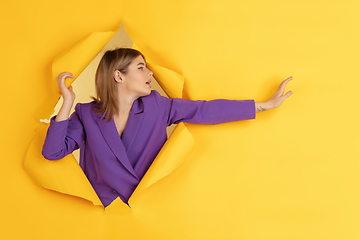 Image showing Cheerful young woman poses in torn yellow paper hole background, emotional and expressive