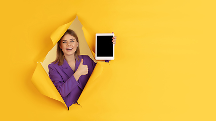 Image showing Cheerful young woman poses in torn yellow paper hole background, emotional and expressive