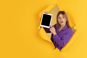 Image showing Cheerful young woman poses in torn yellow paper hole background, emotional and expressive