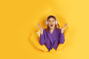 Image showing Cheerful young woman poses in torn yellow paper hole background, emotional and expressive