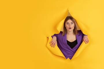 Image showing Cheerful young woman poses in torn yellow paper hole background, emotional and expressive