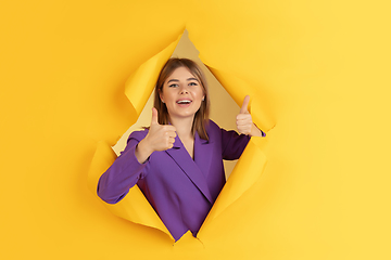 Image showing Cheerful young woman poses in torn yellow paper hole background, emotional and expressive