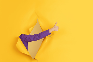 Image showing Female hand gesturing in torn yellow paper hole background