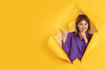 Image showing Cheerful young woman poses in torn yellow paper hole background, emotional and expressive