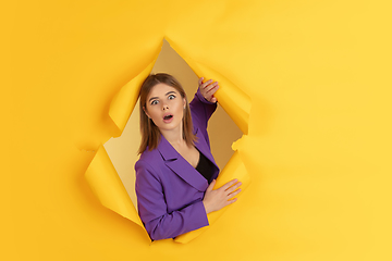 Image showing Cheerful young woman poses in torn yellow paper hole background, emotional and expressive