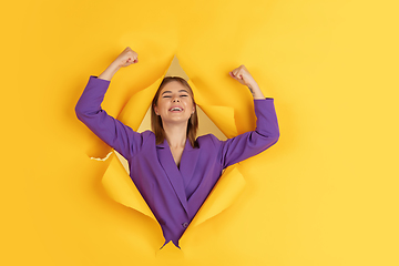 Image showing Cheerful young woman poses in torn yellow paper hole background, emotional and expressive