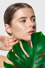 Image showing Inspired. Close up of beautiful young woman with green leaves on her face over white background. Cosmetics and makeup, natural and eco treatment, skin care