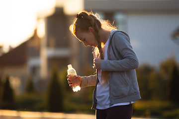 Image showing Young female runner, athlete resting after jogging in the city street in sunshine. Beautiful caucasian woman training, listening to music