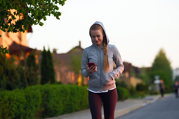 Image showing Young female runner, athlete resting after jogging in the city street in sunshine. Beautiful caucasian woman training, listening to music