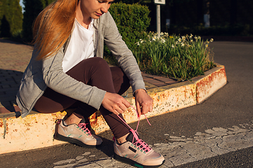 Image showing Young female runner, athlete resting after jogging in the city street in sunshine. Beautiful caucasian woman training, listening to music