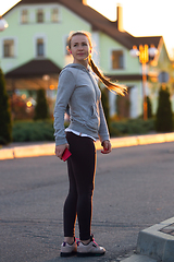 Image showing Young female runner, athlete during jogging in the city street in sunshine. Beautiful caucasian woman training, listening to music