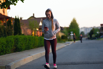 Image showing Young female runner, athlete resting after jogging in the city street in sunshine. Beautiful caucasian woman training, listening to music