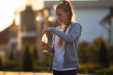 Image showing Young female runner, athlete resting after jogging in the city street in sunshine. Beautiful caucasian woman training, listening to music