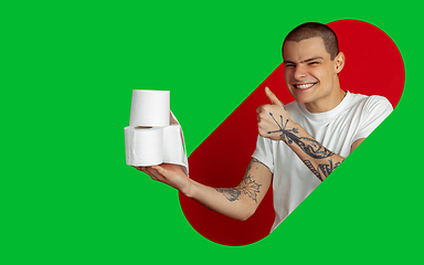 Image showing Portrait of young man on bright bicolor background with geometric style, modern design, artwork. Holding toilet paper, scary smiling and thumb up