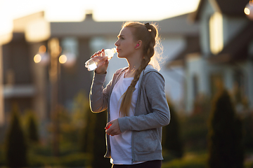 Image showing Young female runner, athlete resting after jogging in the city street in sunshine. Beautiful caucasian woman training, listening to music