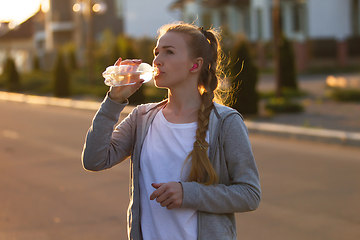 Image showing Young female runner, athlete resting after jogging in the city street in sunshine. Beautiful caucasian woman training, listening to music