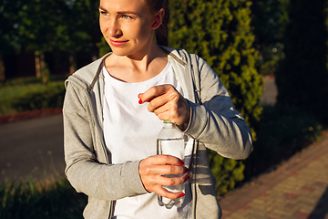 Image showing Young female runner, athlete resting after jogging in the city street in sunshine. Beautiful caucasian woman training, listening to music