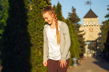 Image showing Young female runner, athlete resting after jogging in the city street in sunshine. Beautiful caucasian woman training, listening to music