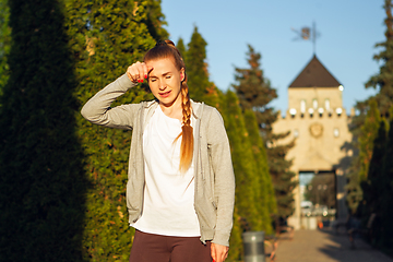 Image showing Young female runner, athlete resting after jogging in the city street in sunshine. Beautiful caucasian woman training, listening to music