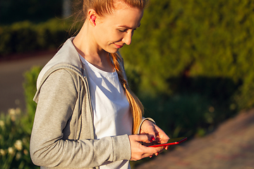 Image showing Young female runner, athlete resting after jogging in the city street in sunshine. Beautiful caucasian woman training, listening to music