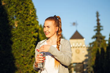 Image showing Young female runner, athlete resting after jogging in the city street in sunshine. Beautiful caucasian woman training, listening to music