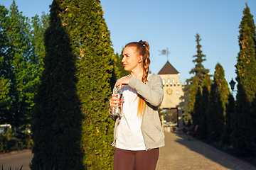 Image showing Young female runner, athlete resting after jogging in the city street in sunshine. Beautiful caucasian woman training, listening to music