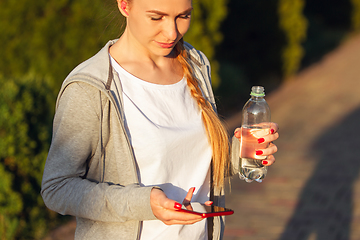 Image showing Young female runner, athlete resting after jogging in the city street in sunshine. Beautiful caucasian woman training, listening to music