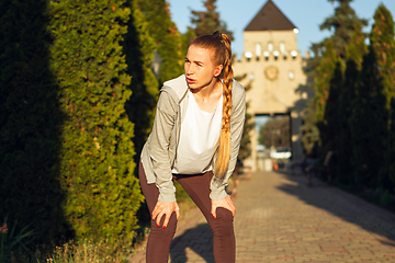 Image showing Young female runner, athlete resting after jogging in the city street in sunshine. Beautiful caucasian woman training, listening to music