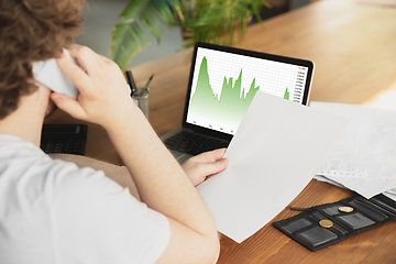 Image showing Caucasian upset and despair man watching financial and economical graphs going down during coronavirus quarantine, problems