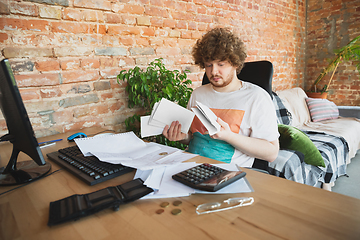 Image showing Caucasian upset and despair man doing financial and economical reports with income going down during coronavirus quarantine, problems