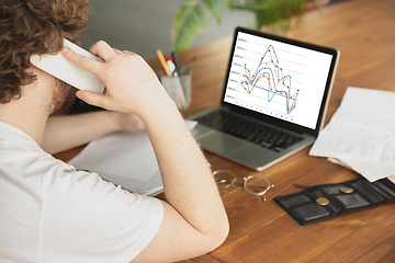 Image showing Caucasian upset and despair man watching financial and economical graphs going down during coronavirus quarantine, problems