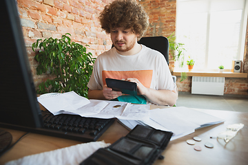 Image showing Caucasian upset and despair man doing financial and economical reports with income going down during coronavirus quarantine, problems