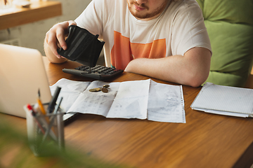 Image showing Caucasian upset and despair man looking in empty wallet during coronavirus quarantine, business fall, lack of money, problems