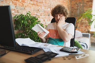 Image showing Caucasian upset and despair man doing financial and economical reports with income going down during coronavirus quarantine, problems