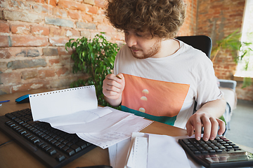 Image showing Caucasian upset and despair man doing financial and economical reports with income going down during coronavirus quarantine, problems