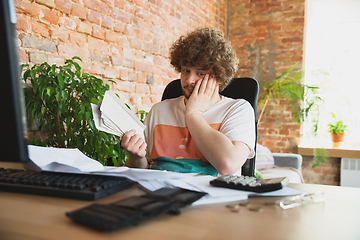 Image showing Caucasian upset and despair man doing financial and economical reports with income going down during coronavirus quarantine, problems