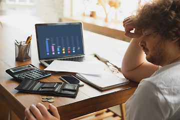 Image showing Caucasian upset and despair man watching financial and economical graphs going down during coronavirus quarantine, problems