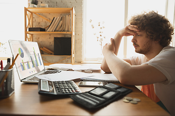 Image showing Caucasian upset and despair man watching financial and economical graphs going down during coronavirus quarantine, problems