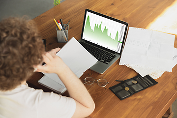 Image showing Caucasian upset and despair man watching financial and economical graphs going down during coronavirus quarantine, problems