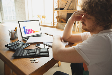 Image showing Caucasian upset and despair man watching financial and economical graphs going down during coronavirus quarantine, problems